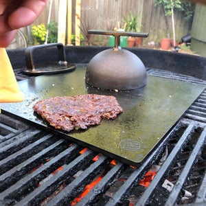 Steel Cloche on a bbq flattop with burger and burger press in shot